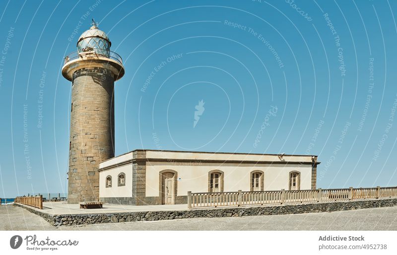 House and beacon on sea shore under blue sky lighthouse construction seashore architecture facade style old island solitude exterior fence high window entrance