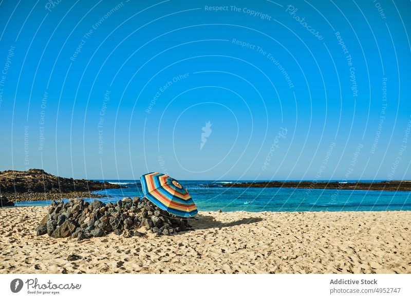 Parasol on sandy sea shore under blue sky nature landscape seascape island horizon parasol untouched stone rocky ocean beach brown color ornament sunshade rough