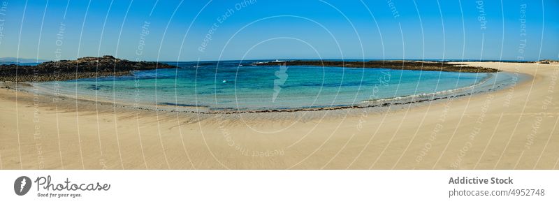 Sandy beach against turquoise sea under blue sky shore ocean seascape nature landscape rock highland untouched island formation horizon shoreline sandy brown