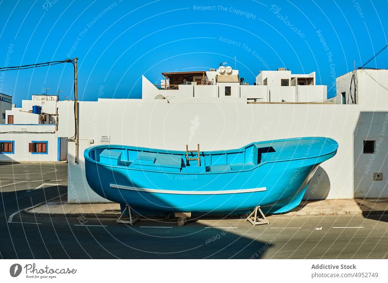 Blue boat on road near buildings in sunlight architecture nautical transport blue sky island moor solitude bright shadow asphalt roadway marking line