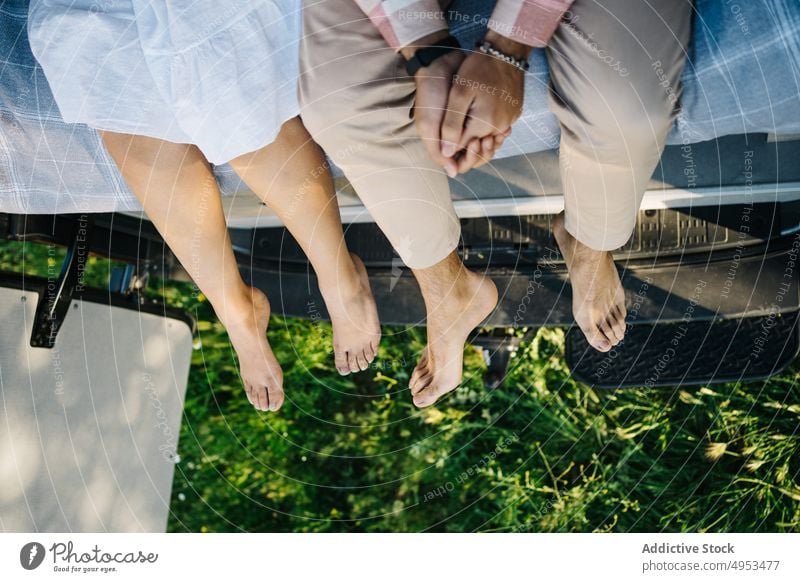 Crop traveling couple sitting on bed in van vacation traveler together caravan barefoot summer trip relationship girlfriend boyfriend carefree automobile parked