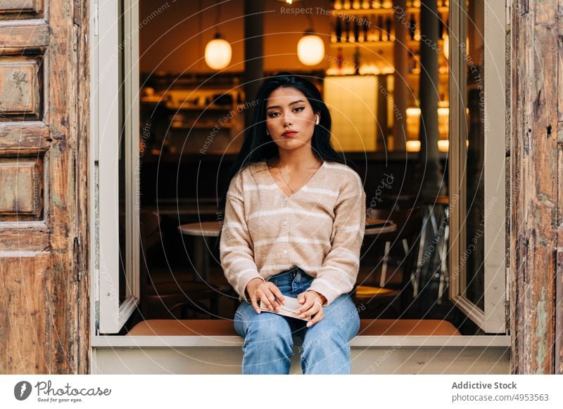 Asian woman in earbuds resting on cafe windowsill feminine style casual romantic dreamy wooden material old weathered contemplate wireless gentle charming