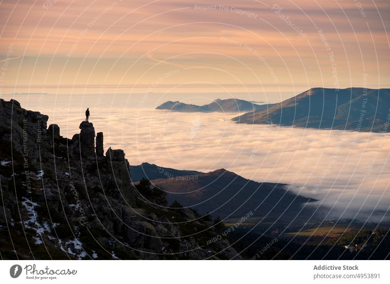 Man standing on high rock and looking at sunset silhouette clouds man mountain sky nature active extreme fog cliff top peak male challenge free courage freedom