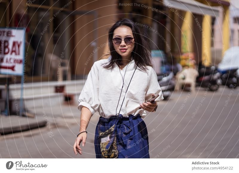 Asian woman walking on old town street ethnic tourist style smartphone pushkar india rajasthan female travel trip pedestrian visit sunglasses trendy confident