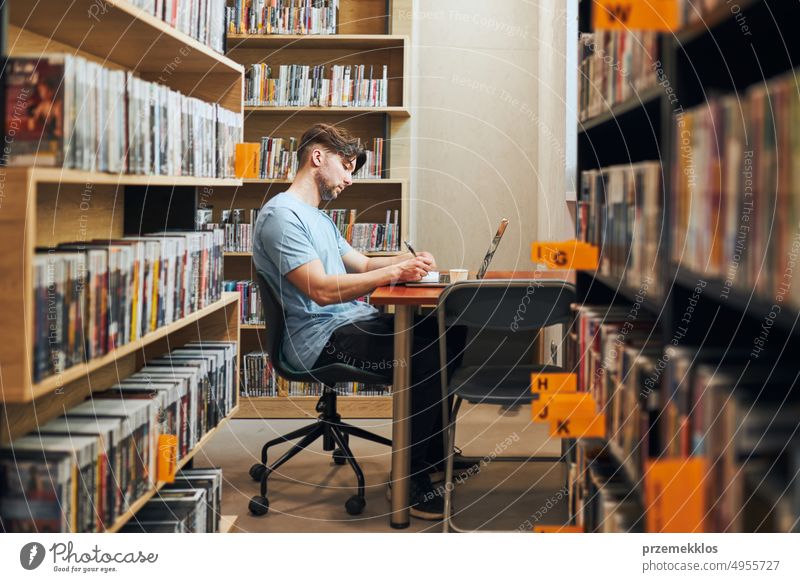 Student studying in the library. Young man prepares for a test on a laptop. Man listening to an online course. Concentrated student studying for college exams.