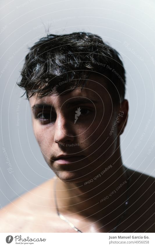 Close-up of a teenager with a serious expression, dark eyes, sweaty skin and contrasted light from above close-up adolescent intrigue mystery shadow wet