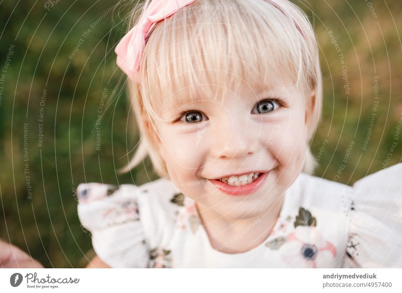 Portrait of a little beautiful girl on nature on summer day vacation. child in dress is playing in the green park at the sunne time. The concept of family holiday and time together