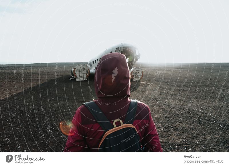 Woman on winter clothes in front of the wreck of th crashed airplane in Iceland, on the beach of Sólheimasandur. Travel to Iceland, road trip concept. Copy space image, visit Iceland.