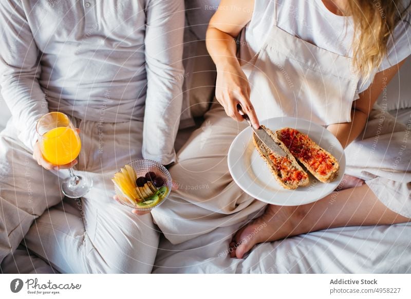 Anonymous couple having breakfast in bedroom happy love morning relationship together honeymoon home beverage drink juice toast jam bonding joy sit affection