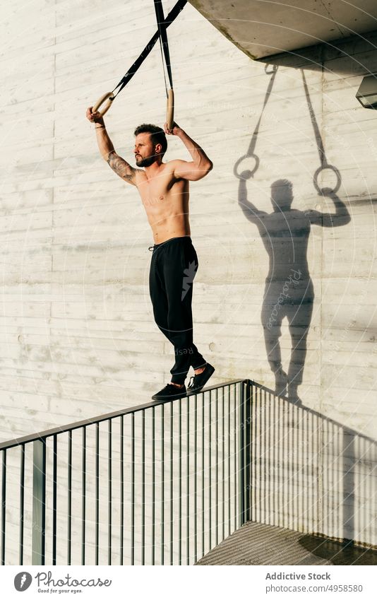 Athletic man balancing on gymnastic rings sportsman shirtless city athletic young active workout construction body lifestyle healthy male exercise fitness