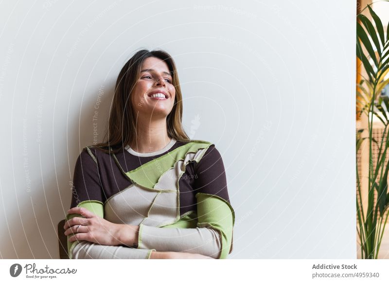 Gentle woman resting on chair smiling looking away contemplate feminine smile gentle charming millennial portrait pleasant sit tropical plant cheerful exotic