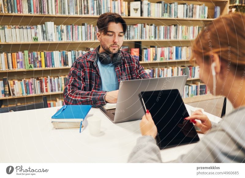 Students learning in university library. Girl writing essay and making notes using technology. Young man having video class on laptop. Students studying for college exams