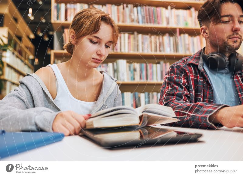 Students learning in university library. Young man preparing for test on laptop. Girl learning from book. Focused students studying for college exams Students discussing and learning together