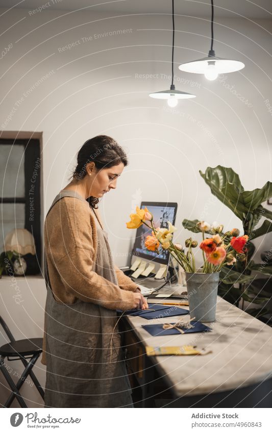 Pensive adult woman making decorative envelopes for selling whil worker shop home workplace creative handmade process design business floral inspiration