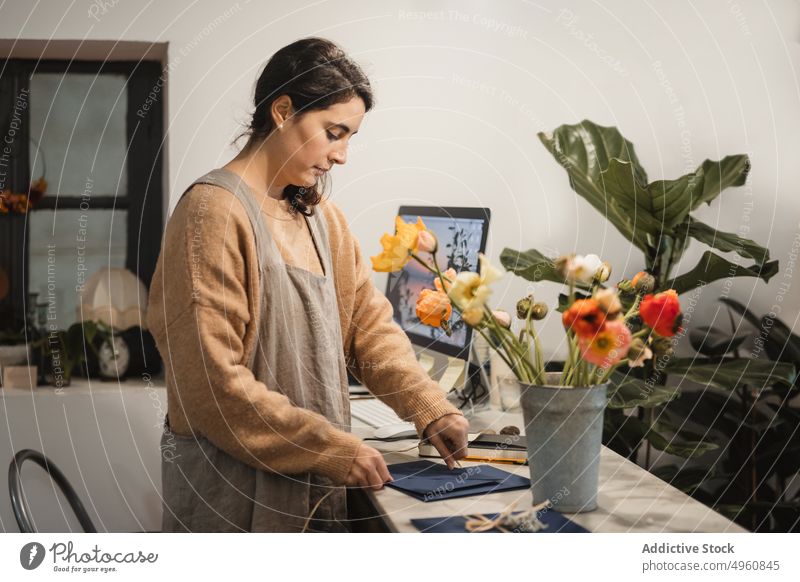 Pensive adult woman making decorative envelopes for selling whil worker shop home workplace creative handmade process design business floral inspiration