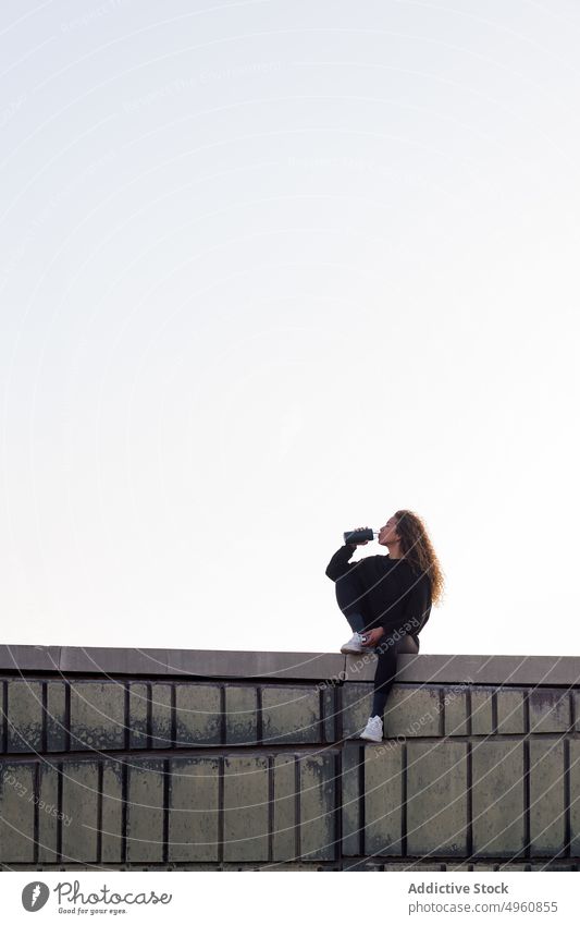 Sportswoman drinking water on construction roof during break from training sportswoman thirsty workout rest sky bottle beverage sneakers sit enjoy athlete