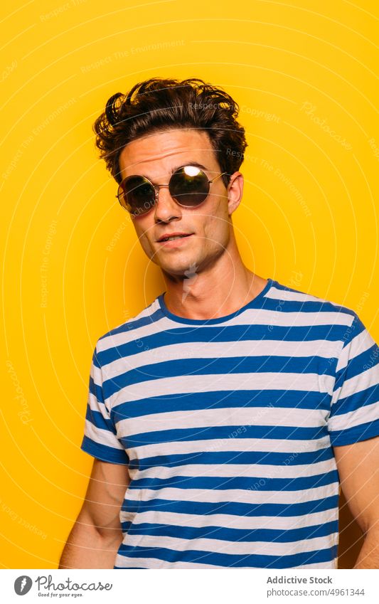 Stylish model with modern haircut on yellow background looking at camera man sunglasses fashion trendy rebel stripe colorful portrait having fun transparent