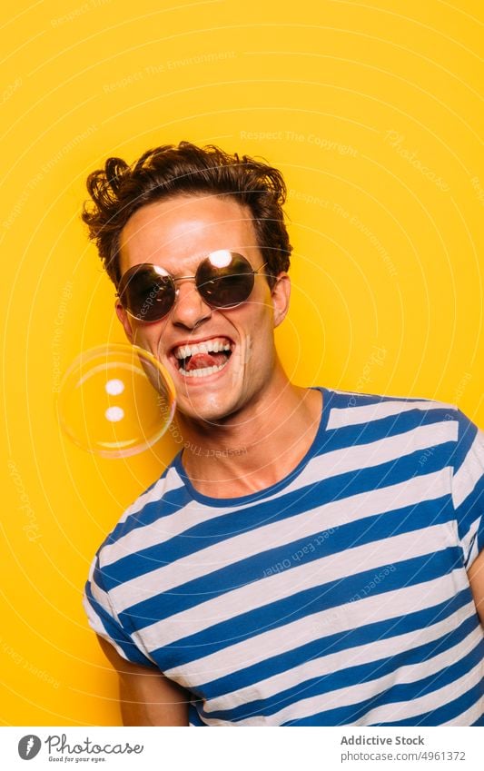 Rebellious man in modern sunglasses against soap bubble fashion trendy tongue out rebel stripe colorful portrait having fun transparent ornament accessory