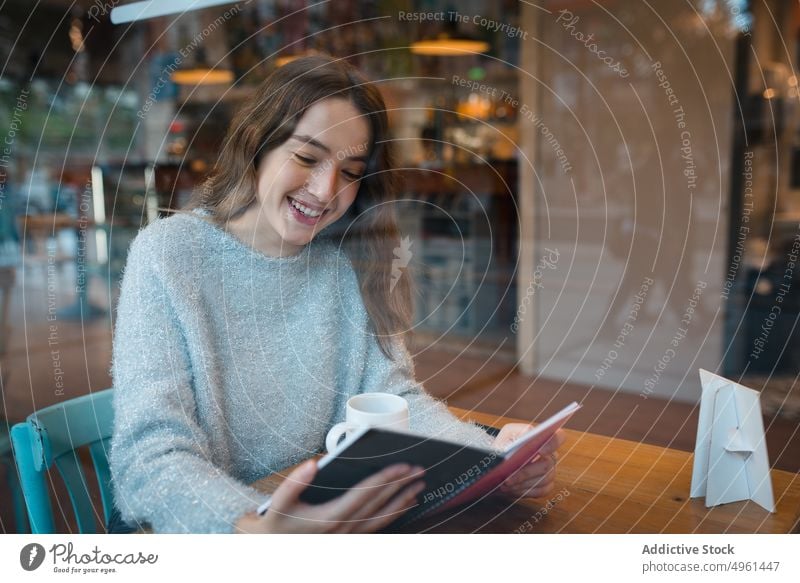 Young woman reading book in cafe cheerful interesting literature enjoy bookworm cafeteria female smile lifestyle sit happy relax table novel fiction story young