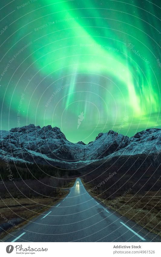 Car on road under green northern lights at night aurora borealis car mountain winter polar scenery sky shiny norway lofoten islands illuminate glow nature