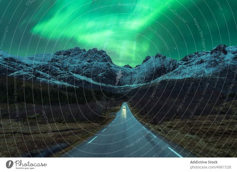 Car on road under green northern lights at night aurora borealis car mountain winter polar scenery sky shiny norway lofoten islands illuminate glow nature