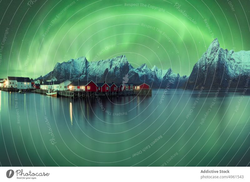 Northern lights above mountainous village near lake aurora borealis northern green highland sky house night lofoten islands norway illuminate glow breathtaking