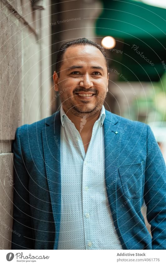 Hispanic businessman standing on old street pavement building suit commute male mature lean middle age smile happy entrepreneur urban weathered glad delight