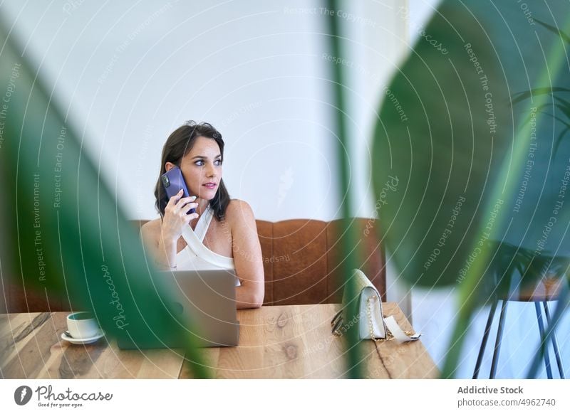 Businesswoman talking on smartphone and browsing laptop during work businesswoman project cafe multitask entrepreneur remote busy freelance mobile focus female