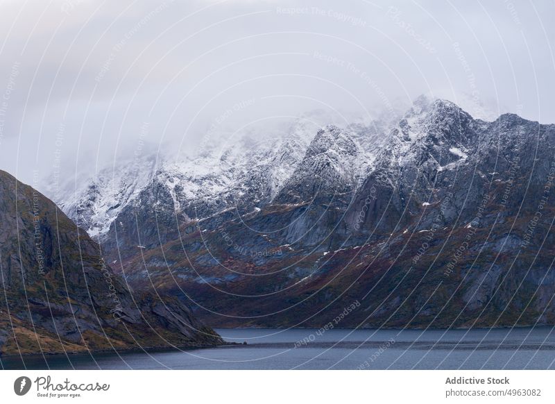 Rocky mountain ridge and wavy sea against gloomy sky in Norway landscape nature cliff snow highland range overcast cloudy massive peak rocky fjord geology reine