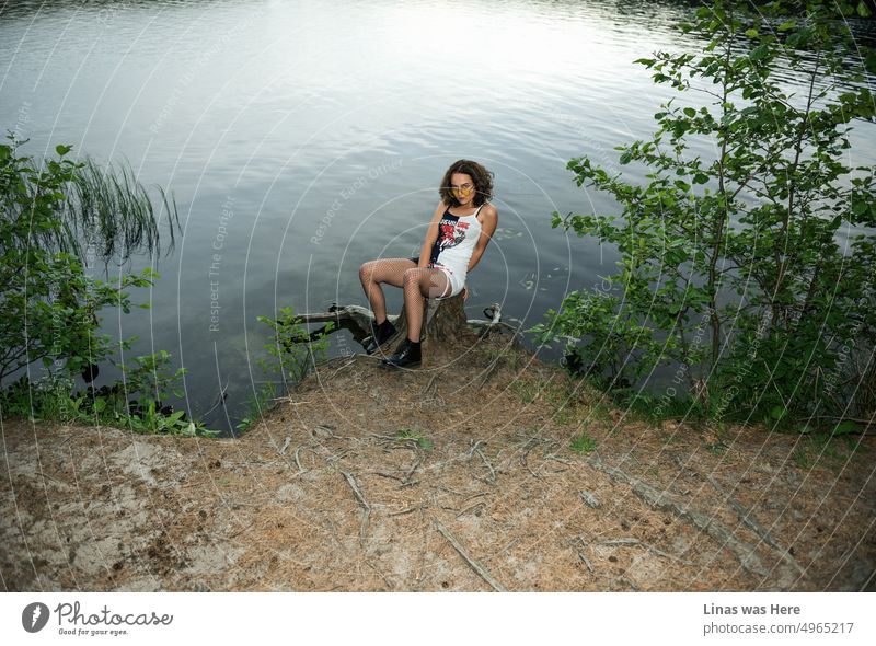 Such a beautiful brunette girl in wild nature. Lake behind her pretty back and roots next to her long legs. A gorgeous fashion model is feeling just fine while flirting with a camera. Killer look!