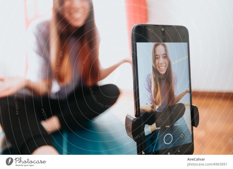 Young woman infuencer explaining yoga positions to followers in front of smart phone, creating social media content. Streaming from home, young people new jobs. Copy space image, mobile phone.