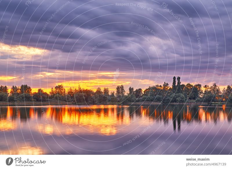 Summer sunset on Lake. Natural rural landscape, autumn September evening. Village on lakeside. Dusk rural scene. Storm cloudscape summer water nature sky