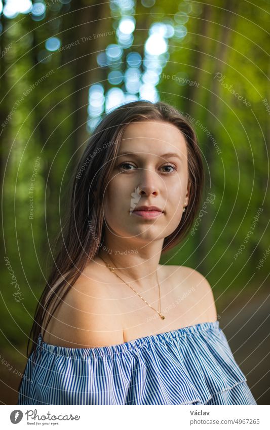 Breathtaking candid portrait of a young brunette in a beautiful summer blue dress on a forest path surrounded by lush summer trees. A measured and ambitious look