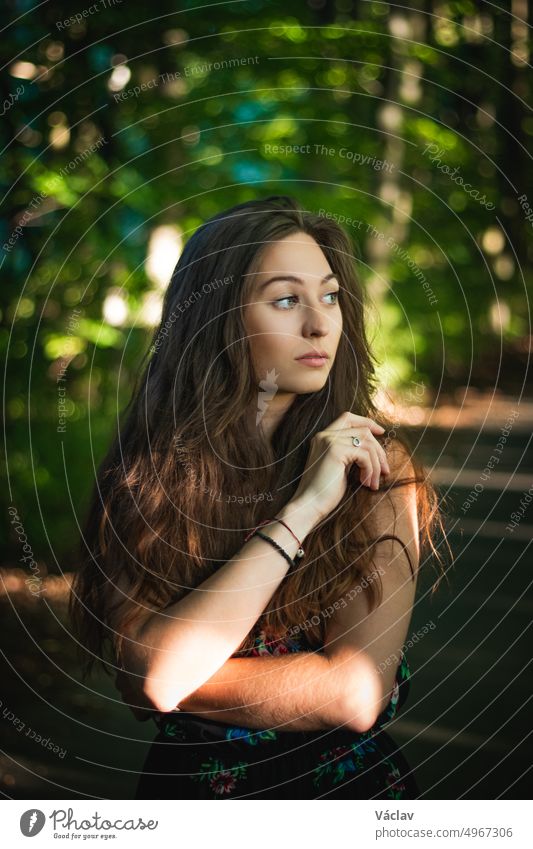 pensive view of a 24 year old woman with dark brown hair in a forest at sunset. Candid portrait of handsome woman in summer dress brunette elegant glamour