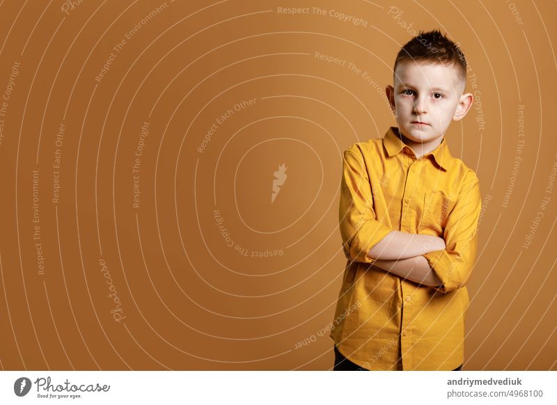 Photo of attractive cheerful nice school boy standing with his arms crossed in front of camera while isolated on yellow background. High quality photo child fun