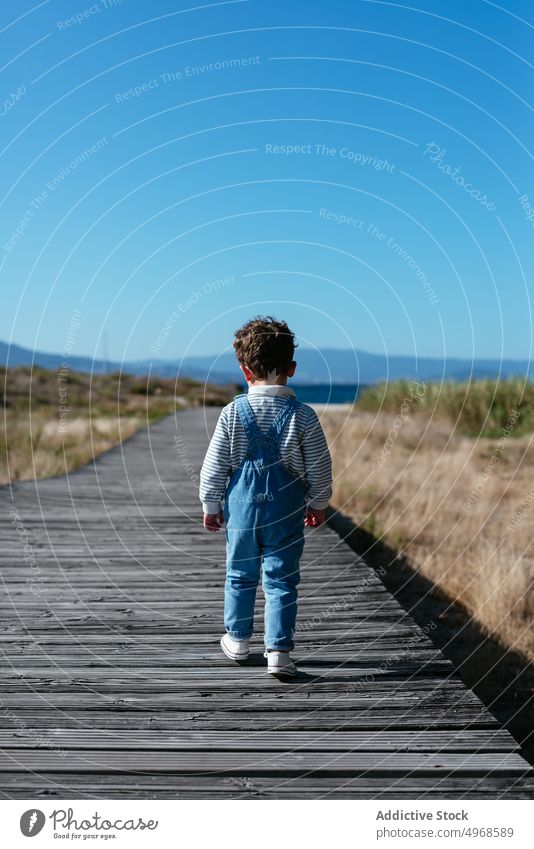 Little boy on boardwalk in field countryside alone summer blue sky carefree walkway stroll path kid child rural idyllic pathway weekend nature childhood little