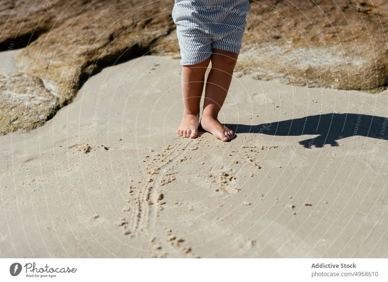 Crop barefoot kid on sandy beach child shoreline summer childhood wet feet nature seashore coast little harmony stand vacation carefree sunlight idyllic calm