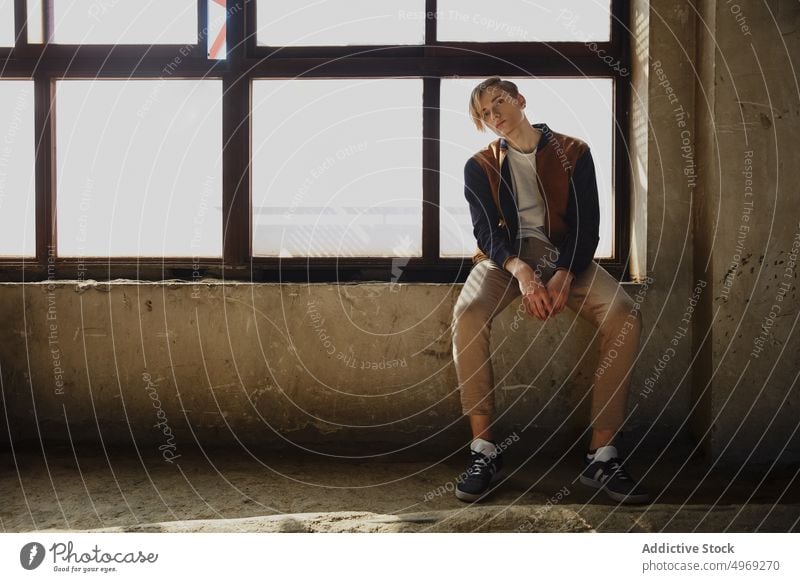 Young man sitting near window in old room windowsill hall handsome relaxed urban trendy cool glamour stylish model young male guy attractive elegance confidence