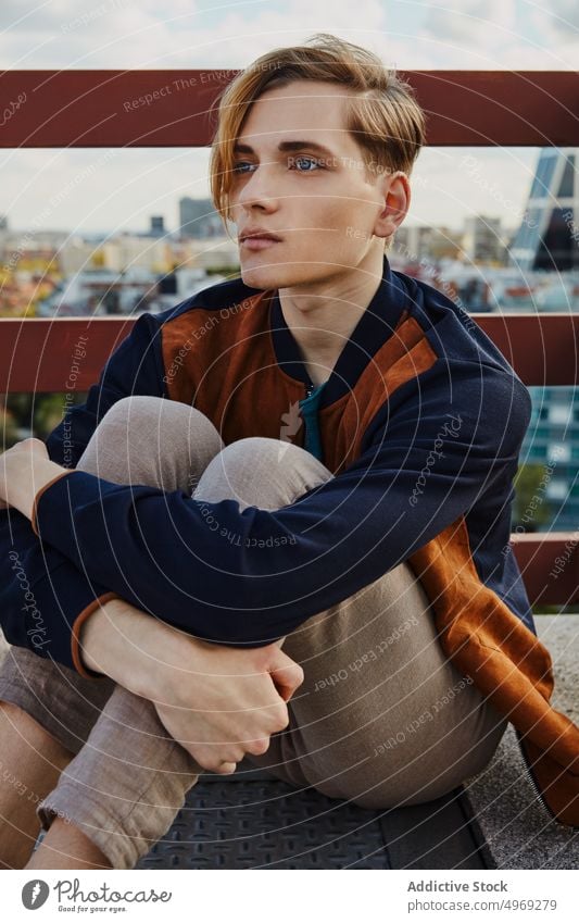 Young blond male sitting on roof of building man handsome relaxed urban trendy stylish model vogue young glamour cool elegance guy confidence attractive happy