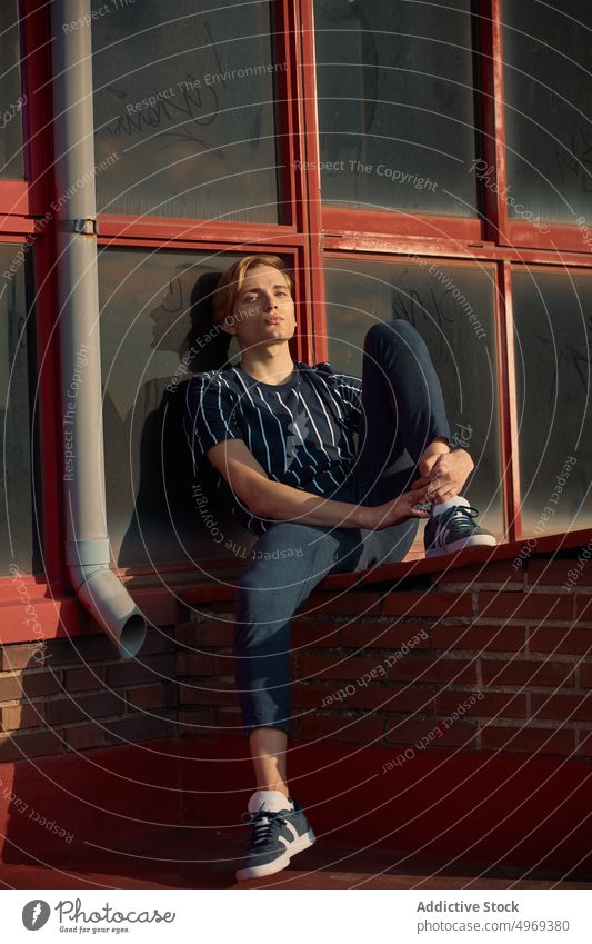 Handsome young male sitting on roof man building street handsome relaxed urban trendy stylish model summer blond attractive happy serious mature fashionable