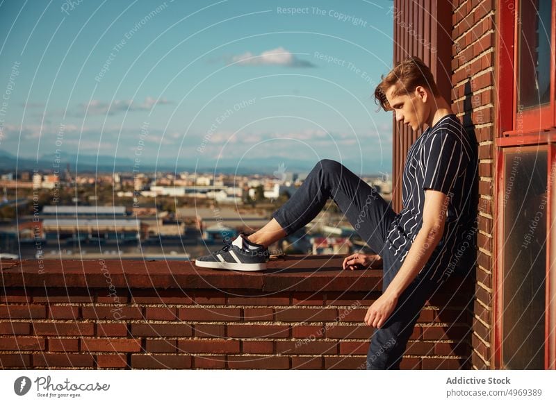 Handsome young male sitting on roof man building street handsome relaxed urban trendy stylish model summer blond attractive happy serious mature fashionable