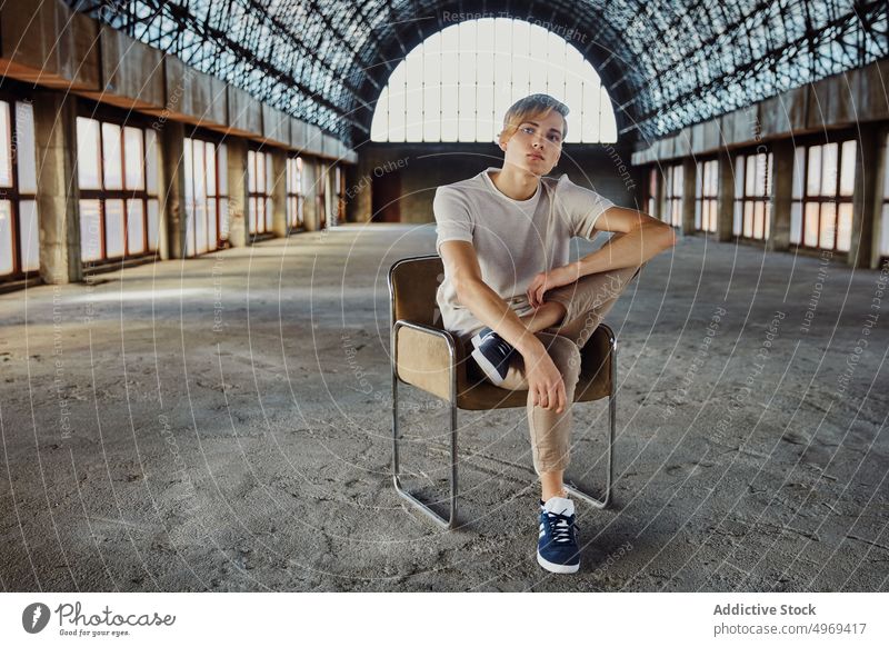 Young trendy man sitting on chair in hall empty handsome relaxed urban glamour cool elegance stylish confidence vogue model young male guy attractive happy