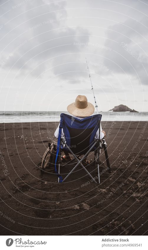 Unrecognizable fisherman preparing fishing rod on seashore coast hobby equipment leisure seaside male hat angler skill water lifestyle line rest free time guy