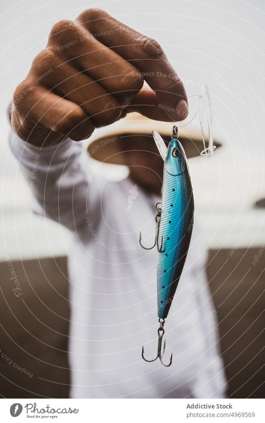 Unrecognizable fisherman with plug in hand blue fishing tackle lure coast shore supply hobby equipment prepare male seashore seaside hat angler skill lifestyle