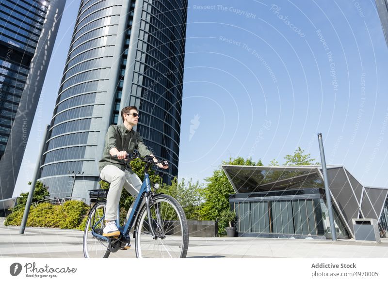 Stylish man riding bike in city center ride bicycle commute work summer urban street male modern businessman transport vehicle sunlight serious guy active