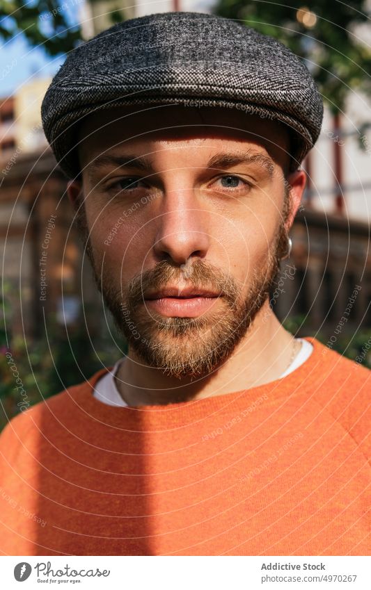 Thoughtful man standing on street near post pillar building city street style portrait urban trendy male beard cap contemporary modern pensive serious town