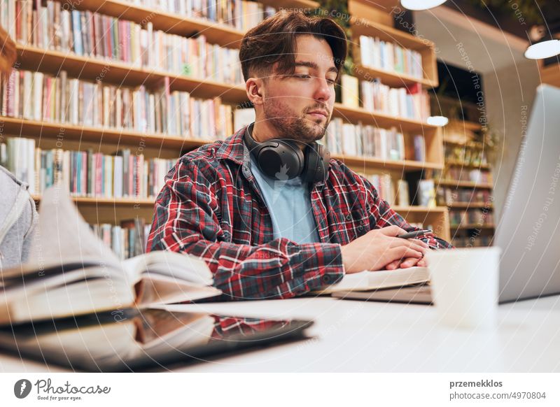 Students learning in university library. Young man preparing for test on laptop. Girl learning from book. Focused students studying for college exams Students discussing and learning together