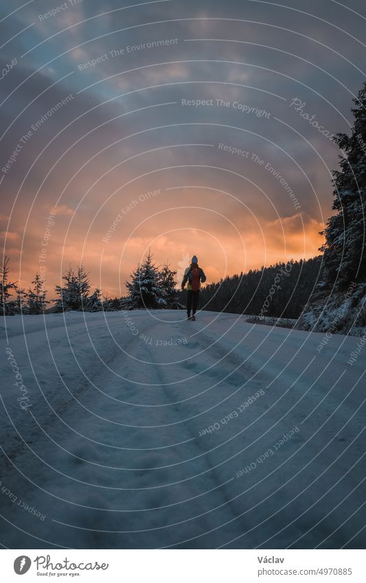 Candid portrait of a man in winter clothes standing at the end of a path watching the sunrise in the snowy area of Stare Hamry Beskydy mountains, Czech republic