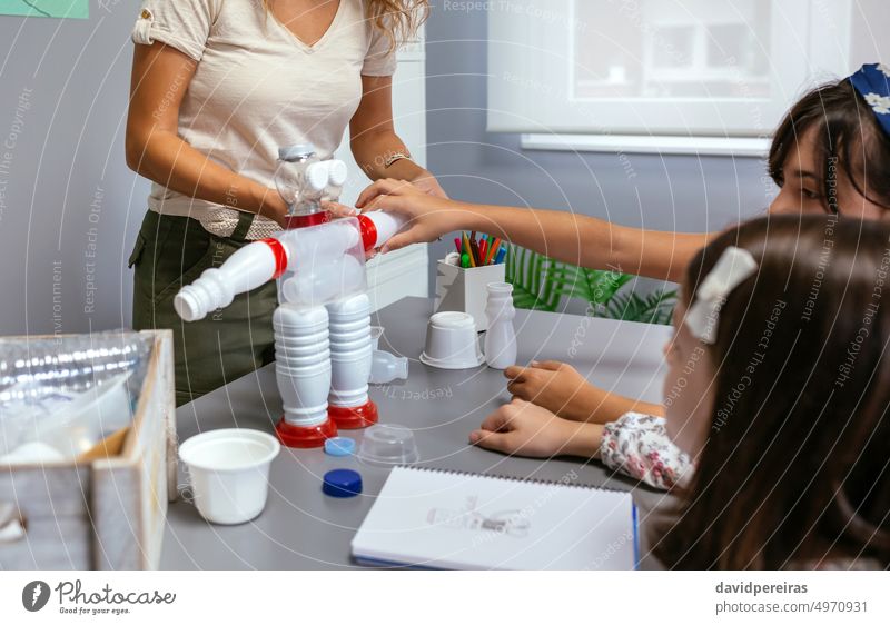 Student putting a piece in recycled toy robot made with plastic packages kid children robotic reuse reduce female girl hand teacher ecology classroom education