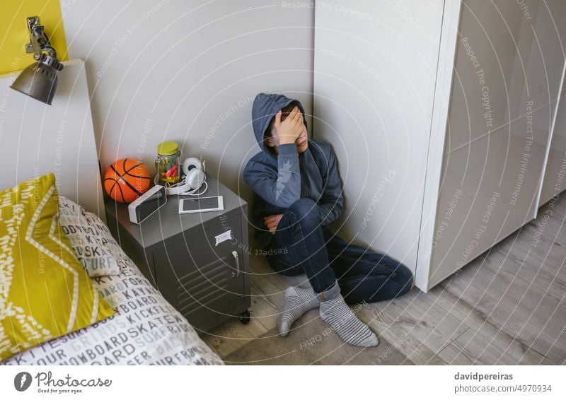 Depressed male teenager sitting on the floor in his bedroom unrecognizable depressed adolescent sad hand head depression stress mental health problem bullying